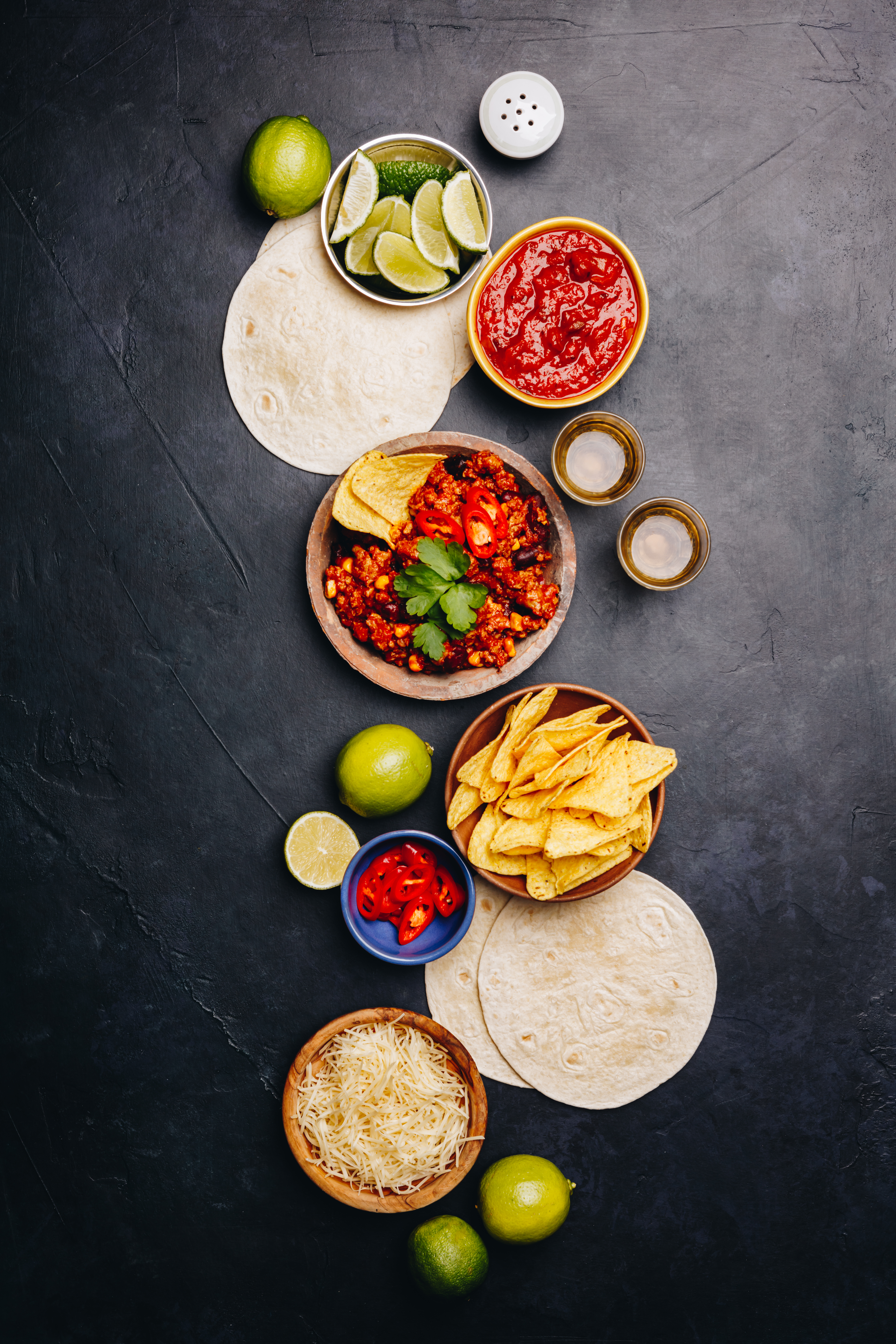 Concept of Mexican food (corn tortillas, nachos, salsa, avocado, limes, cheese, chili con carne) flat lay